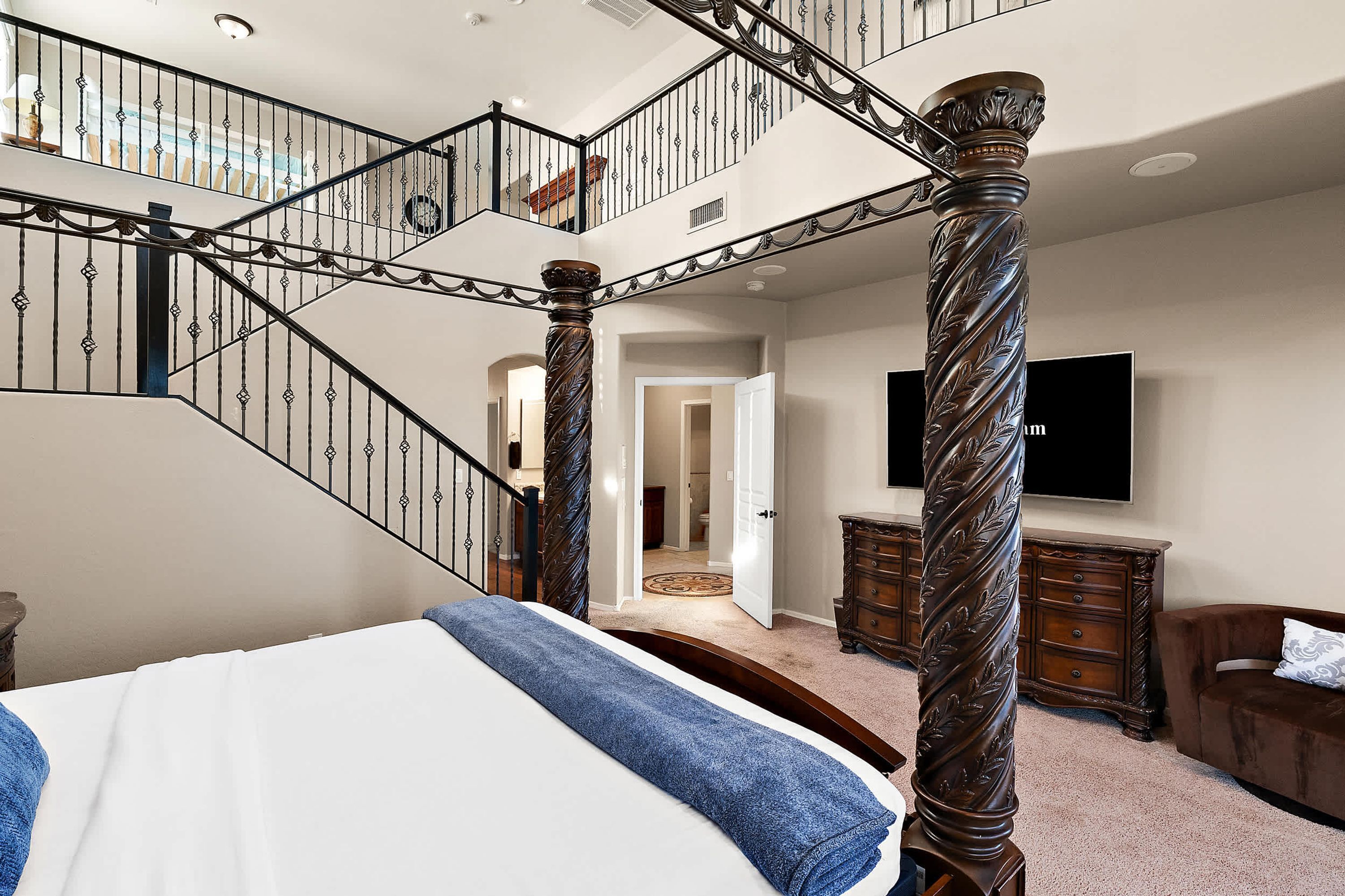 A bedroom with a large bed, a wooden dresser, and a staircase with ornate railings.