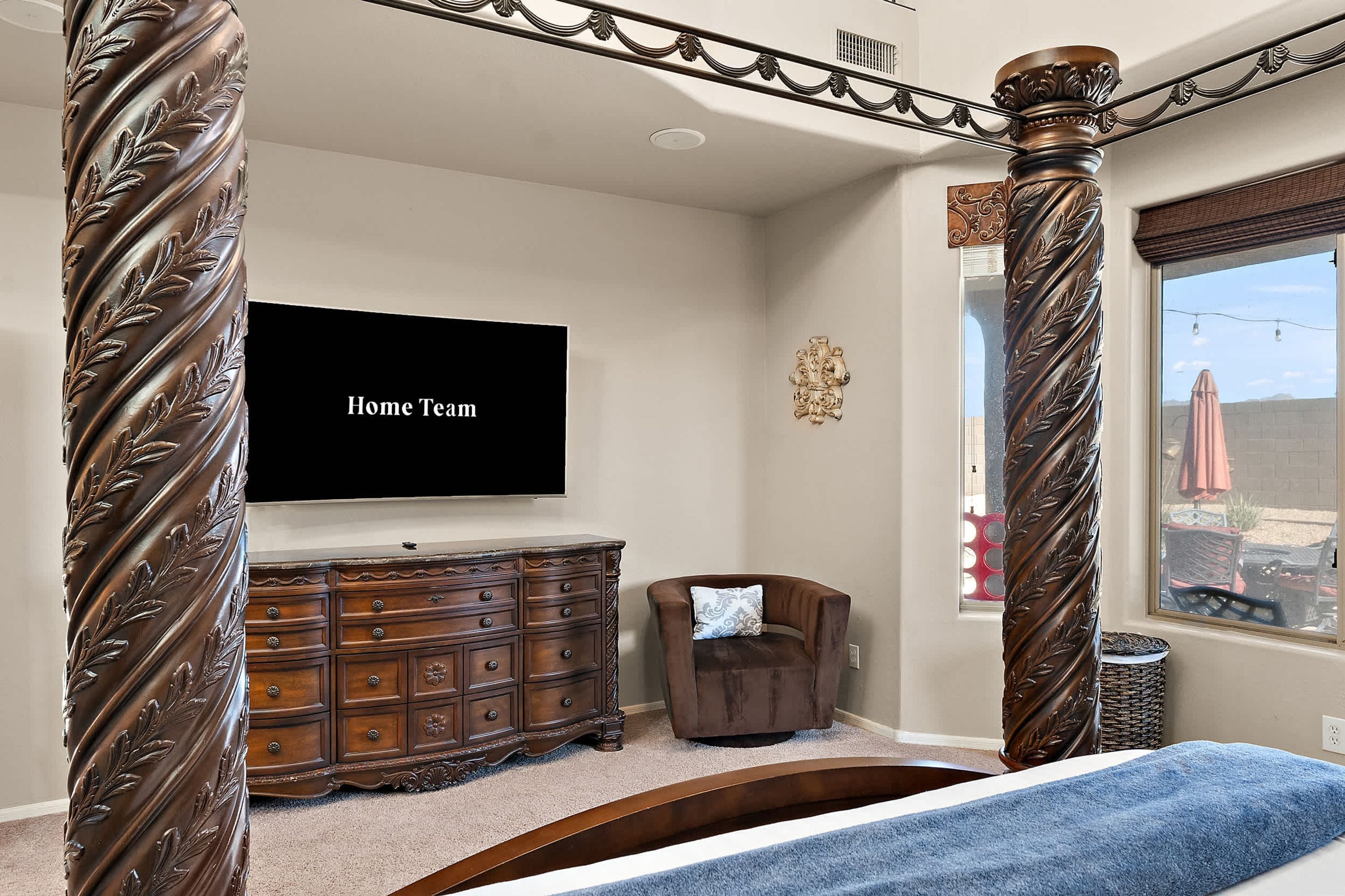 A bedroom with a large bed, a dresser, a TV on the wall, and a window with a view.