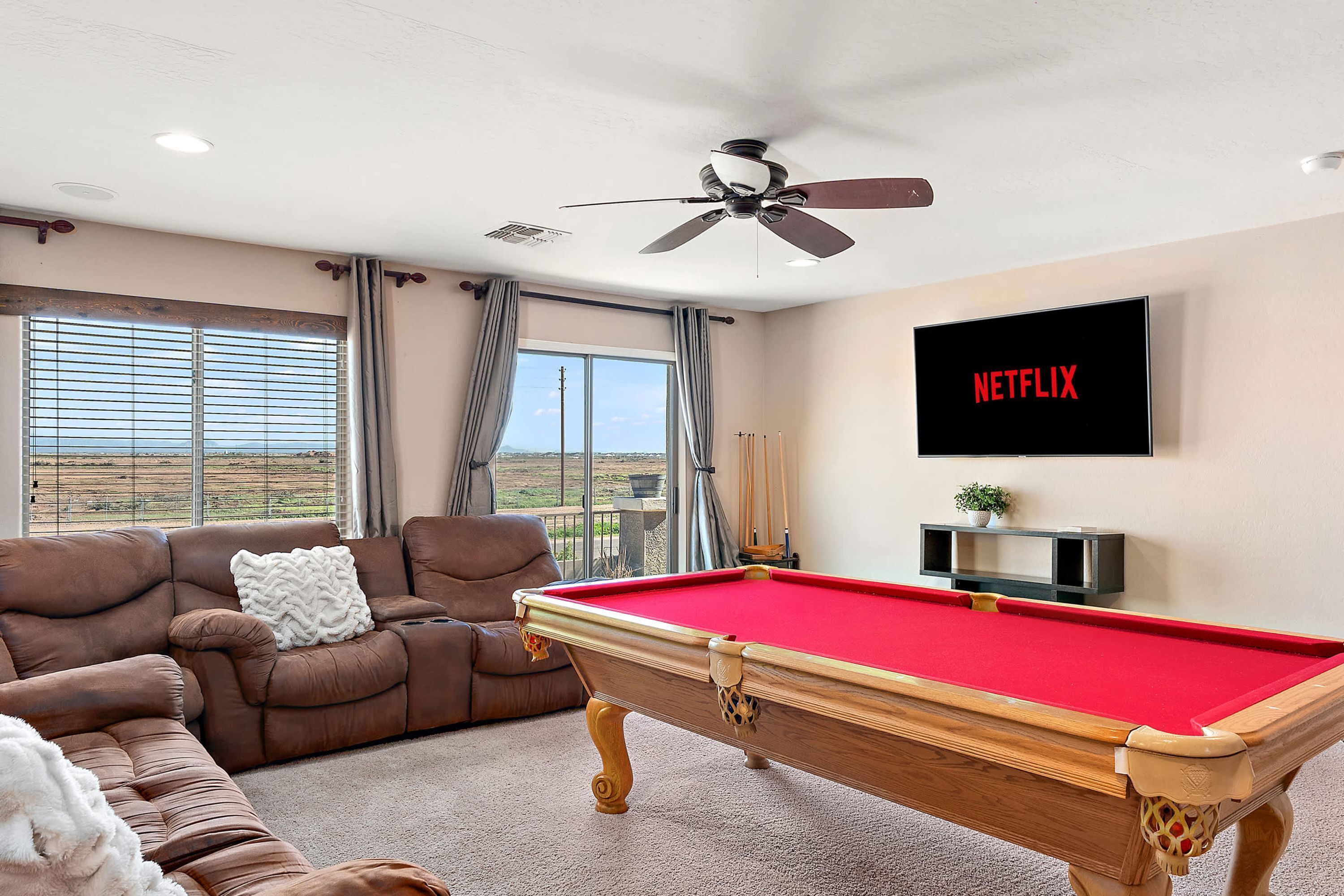A living room with a pool table, a sofa, a television, and a view of the outdoors.
