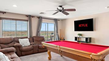 A living room with a pool table, a sofa, a television, and a view of the outdoors.