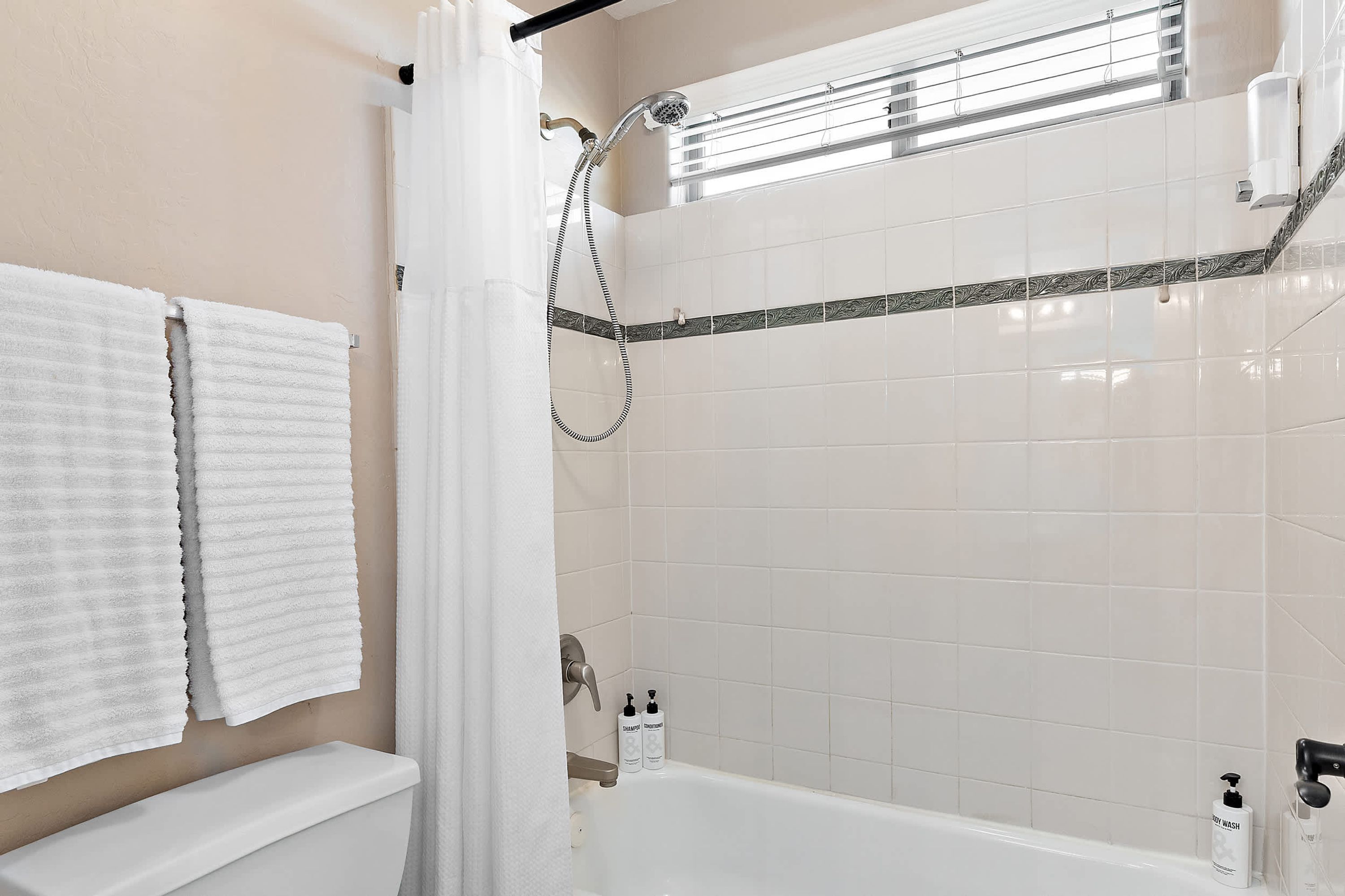 Un baño con bañera, ducha e inodoro. Hay dos toallas blancas colgadas en la pared.
