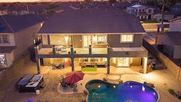 A two-story house with a backyard swimming pool, a patio with outdoor furniture, and a balcony with a table and chairs.