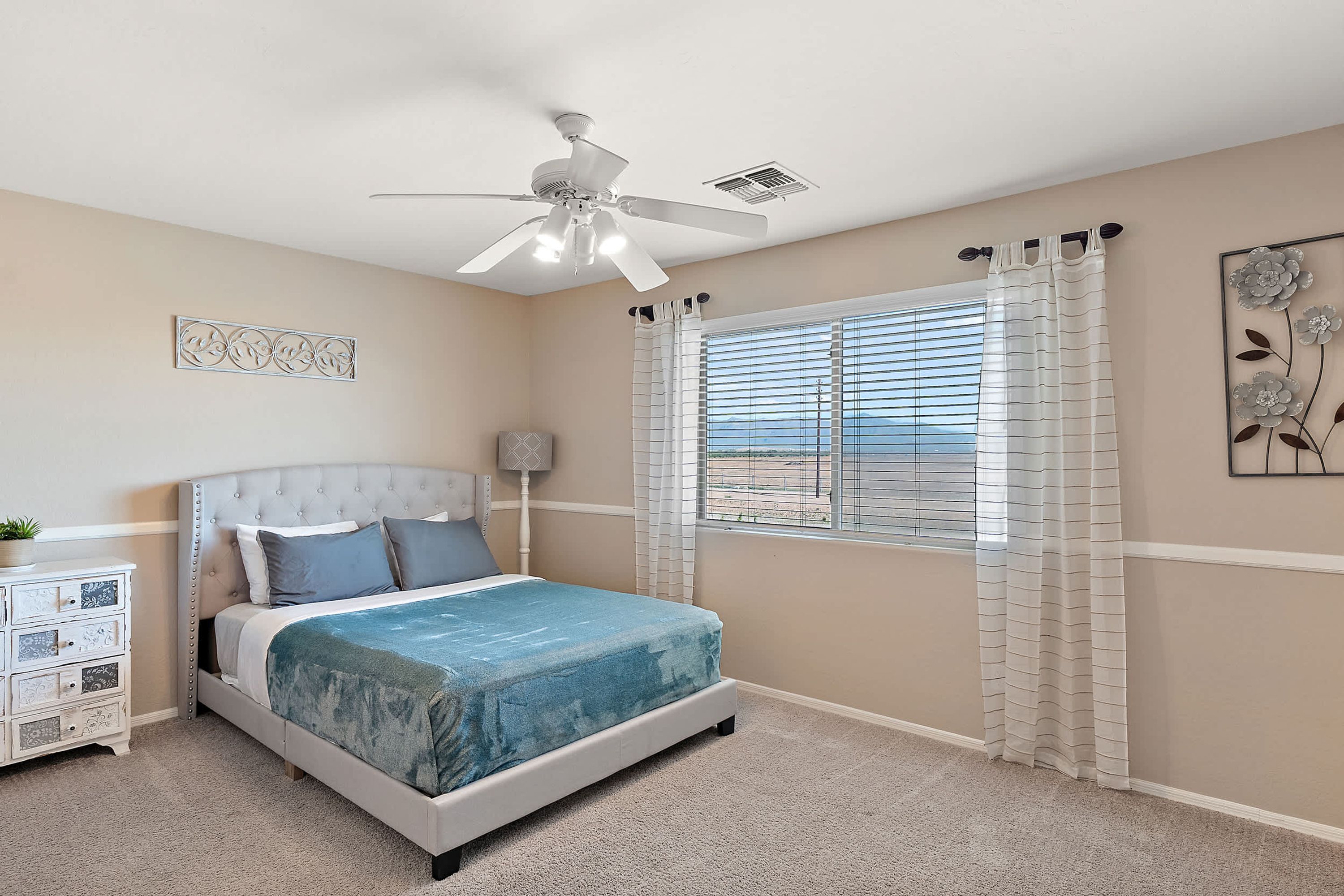 A bedroom with a bed, a nightstand, a ceiling fan, a window with blinds, and a decorative wall piece.