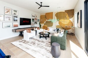 A modern living room with a flat-screen TV, a ceiling fan, and a variety of framed pictures on the wall. - Old Town Estate Pool Theater Game Room (Scottsdale)
