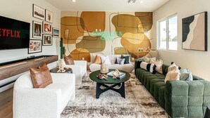 Ein modernes Wohnzimmer mit Flachbildfernseher, Couchtisch, Sofas und einem großen abstrakten Wandbild.