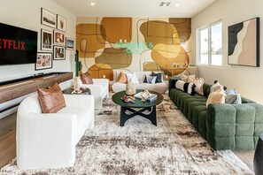 A modern living room with a flat-screen TV, a coffee table, sofas, and a large abstract wall art piece. - Old Town Estate Pool Theater Game Room (Scottsdale)
