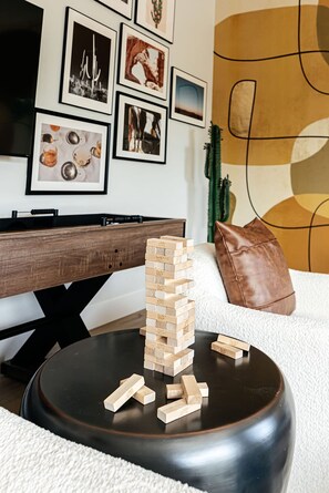 A living room with a wooden Jenga tower on a black coffee table, a white sofa, a brown leather pillow, and a TV on a wooden stand. - Old Town Estate Pool Theater Game Room (Scottsdale)