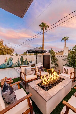 An outdoor patio area with a fire pit, seating, and a cactus wall. - Old Town Estate Pool Theater Game Room (Scottsdale)