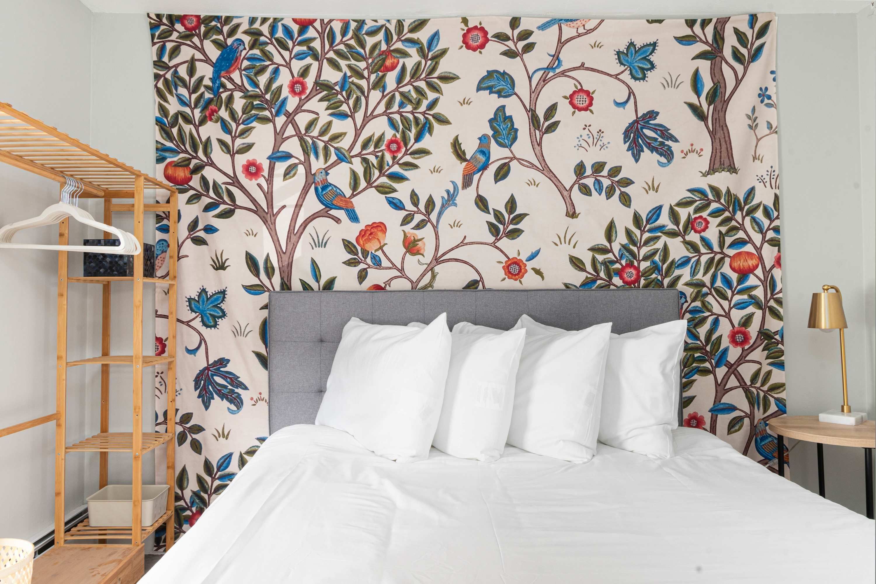 A bedroom with a bed, a wooden shelf unit, and a wall with a floral pattern.
