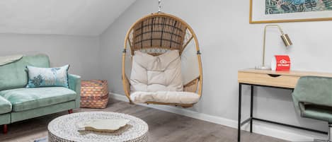 Una habitación acogedora con una silla colgante, un escritorio, un banco acolchado y una mesa redonda con un mantel estampado.