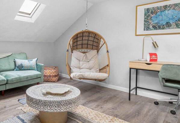 A cozy room with a hanging chair, a desk, a cushioned bench, and a round table with a patterned cover.