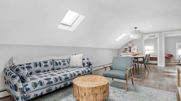 Un loft moderno con soffitto alto, un tavolo da pranzo in legno, un divano blu con cuscini decorati e uno sgabello rotondo in legno.
