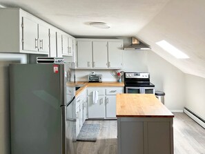 A modern kitchen with white cabinets, a stainless steel refrigerator, a built-in oven, and a wooden countertop.