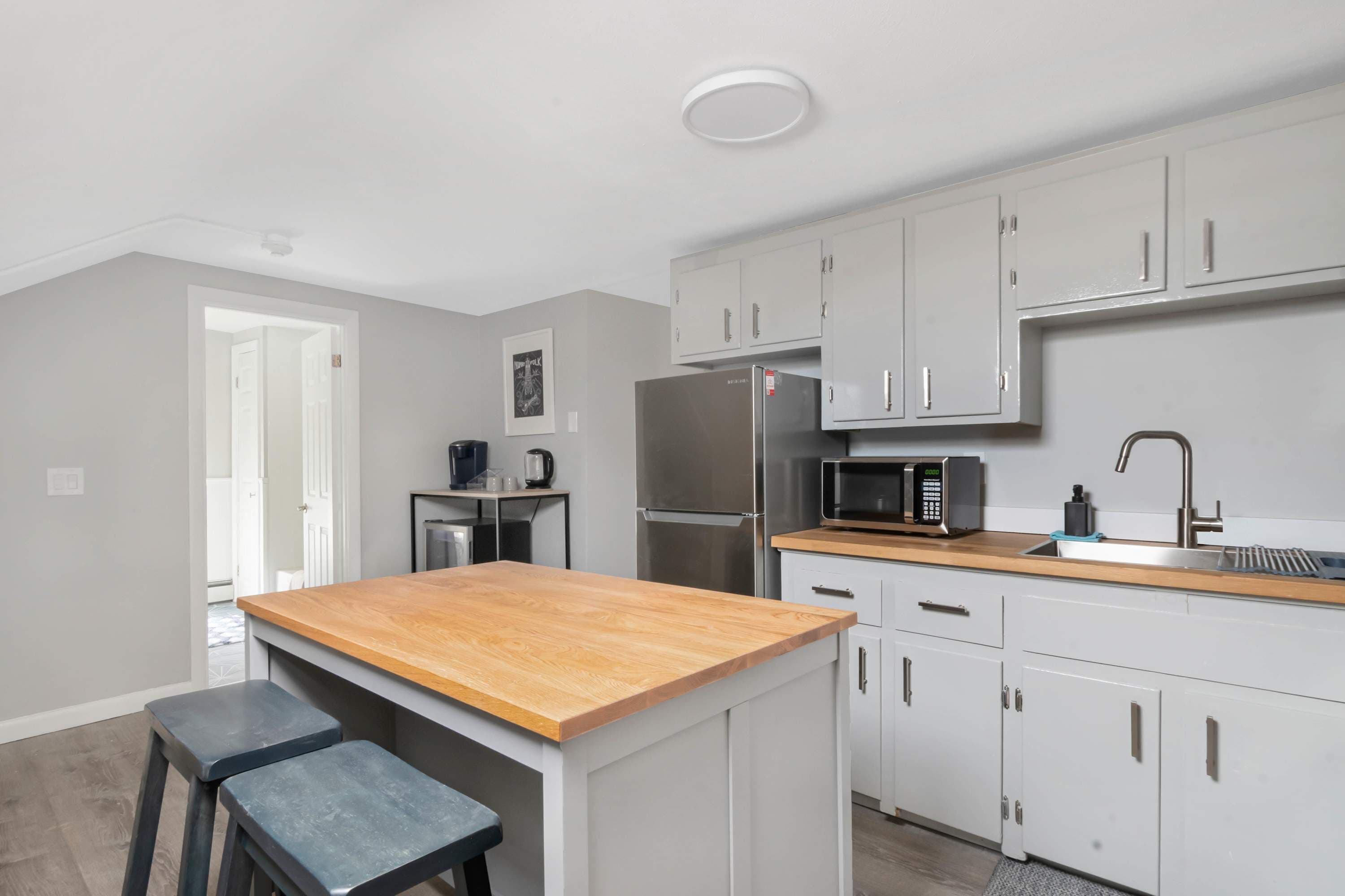 A modern kitchen with white cabinets, a stainless steel refrigerator, a microwave, and a wooden countertop.
