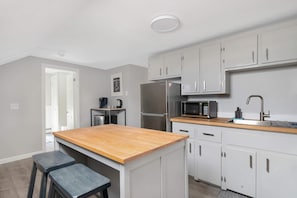 Una cocina moderna con armarios blancos, un refrigerador de acero inoxidable, un microondas y una encimera de madera.