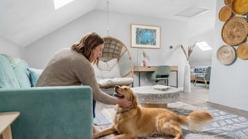 Una persona acariciando a un perro en una habitación con techos altos, una silla colgante, una mesa de comedor y un muro con cestas tejidas.