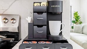 Ett modernt kök med en Keurig-kaffemaskin, ett fack för kaffekapslar och en vit mugg.
