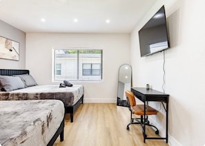 A bedroom with two beds, a desk, a chair, a TV, and a window with blinds. - 3bed Near Wynwood Design District, Beach, Brickell (Miami)