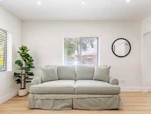 A room with a light-colored sofa, a potted plant, and a wall-mounted mirror. - 3bed Near Wynwood Design District, Beach, Brickell (Miami)