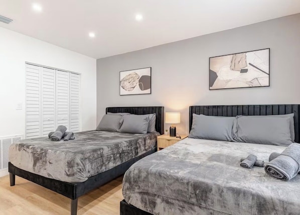 Un dormitorio con dos camas, una mesita de noche con lámpara y una obra de arte en la pared.