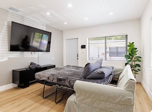 A modern bedroom with a bed, a TV mounted on the wall, a bedside table, a window with blinds, and a potted plant. - 3bed Near Wynwood Design District, Beach, Brickell (Miami)