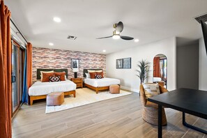 A modern bedroom with two beds, a ceiling fan, a dining table, and a large mirror. - The Desert Reserve Pool Sport Court 7BR (Scottsdale)