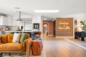 A modern kitchen with stainless steel appliances, a dining area with a brown leather couch, and a living room with a geometric coffee table. - The Desert Reserve Pool Sport Court 7BR (Scottsdale)