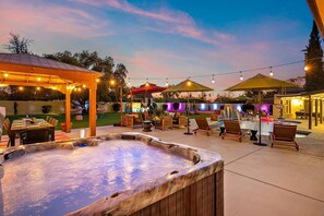 An outdoor patio area with a hot tub, lounge chairs, and string lights. - The Desert Reserve Pool Sport Court 7BR (Scottsdale)
