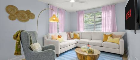 A living room with a grey armchair, a white sectional sofa, a round wooden coffee table, and a ceiling fan.