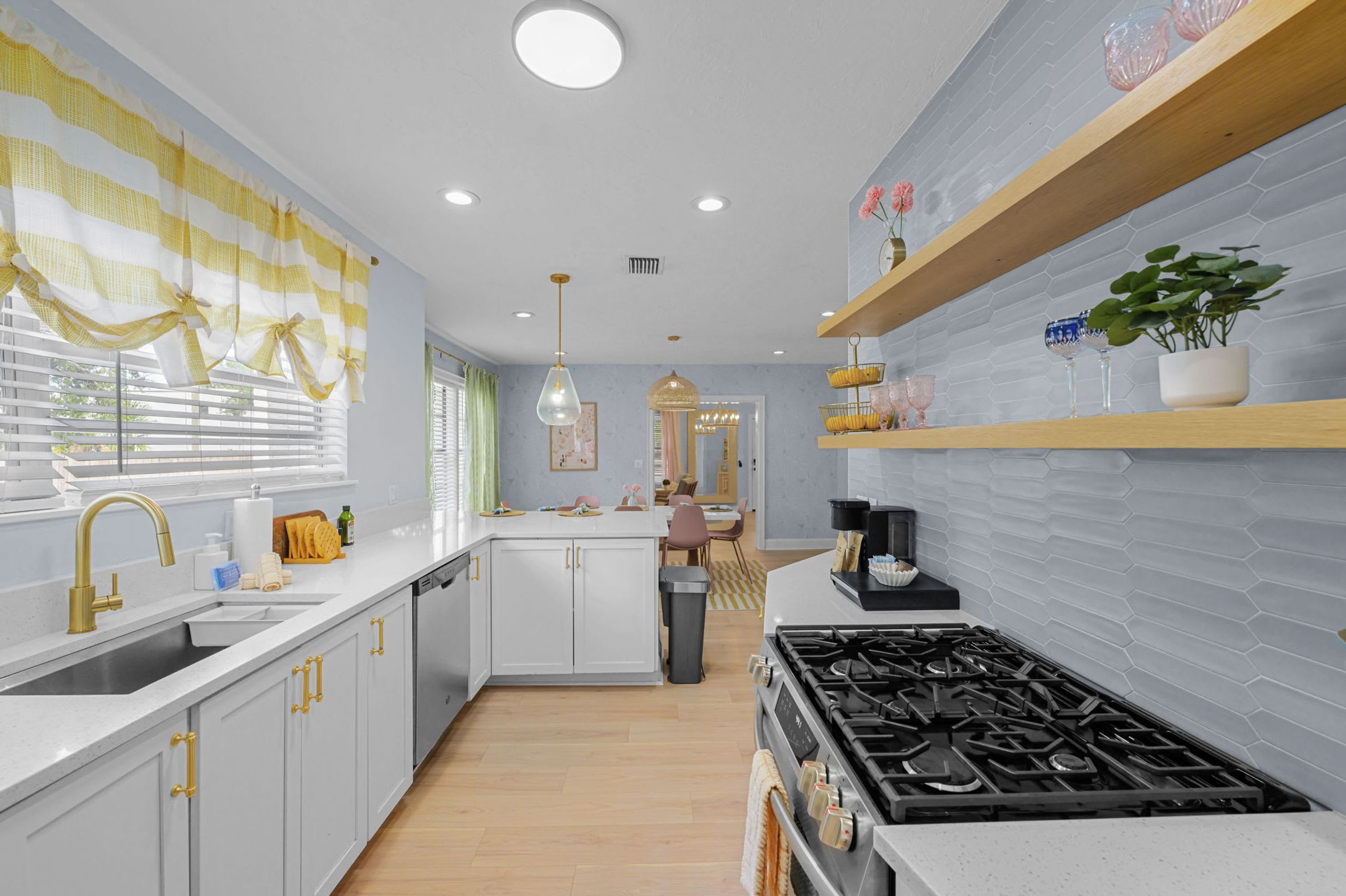 Una cucina moderna con mobili bianchi, un fornello a gas e uno scaffale in legno con oggetti decorativi.