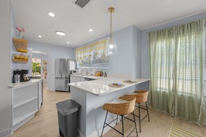 A modern kitchen with a central island, bar stools, a trash bin, and a view of the adjacent living area. - Bradenton Bliss Heated Pool Hot Tub Games (Bradenton)