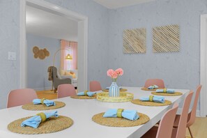 Ein Essbereich mit einem weißen Tisch, gedeckt für sechs Personen, umgeben von rosa Stühlen. In der Mitte steht eine Blumenvase.