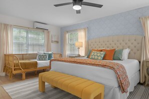 Ein Schlafzimmer mit Bett, einer Bank, einem Nachttisch, einer Lampe und einem Deckenventilator.
