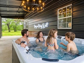 A hot tub with four people, a neon sign, and a view of trees. - Stillstone Ranch A Wellness Retreat Sleeps 32 (Driftwood)