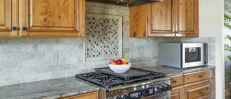 A kitchen with wooden cabinets, a stainless steel range hood, a microwave, and a bowl of fruit on the counter.