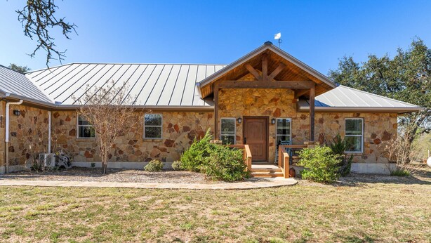 A stone house with a metal roof, a wooden front porch, and a small garden. - Stillstone Ranch A Wellness Retreat Sleeps 32 (Driftwood)