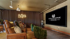 A modern living room with leather sofas, a large flat-screen TV, and a neon sign. - Stillstone Ranch A Wellness Retreat Sleeps 32 (Driftwood)