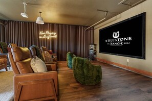 A modern living room with leather sofas, a large flat-screen TV, and a neon sign. - Stillstone Ranch A Wellness Retreat Sleeps 32 (Driftwood)
