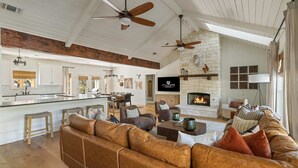 A spacious living room with a leather sofa, a fireplace, and a stone wall. - Stillstone Ranch A Wellness Retreat Sleeps 32 (Driftwood)