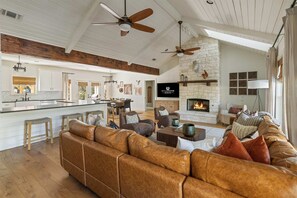 A spacious living room with a leather sofa, a fireplace, and a stone wall. - Stillstone Ranch A Wellness Retreat Sleeps 32 (Driftwood)