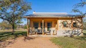 A single-story house with a covered porch, a small garden, and a clear sky. - Stillstone Ranch A Wellness Retreat Sleeps 32 (Driftwood)