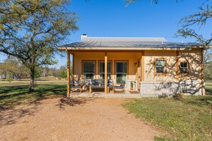 A single-story house with a covered porch, a small garden, and a clear sky. - Stillstone Ranch A Wellness Retreat Sleeps 32 (Driftwood)