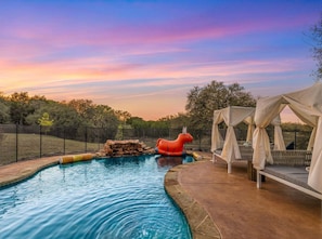 A swimming pool with a slide, a covered seating area, and a sunset in the background. - Stillstone Ranch A Wellness Retreat Sleeps 32 (Driftwood)