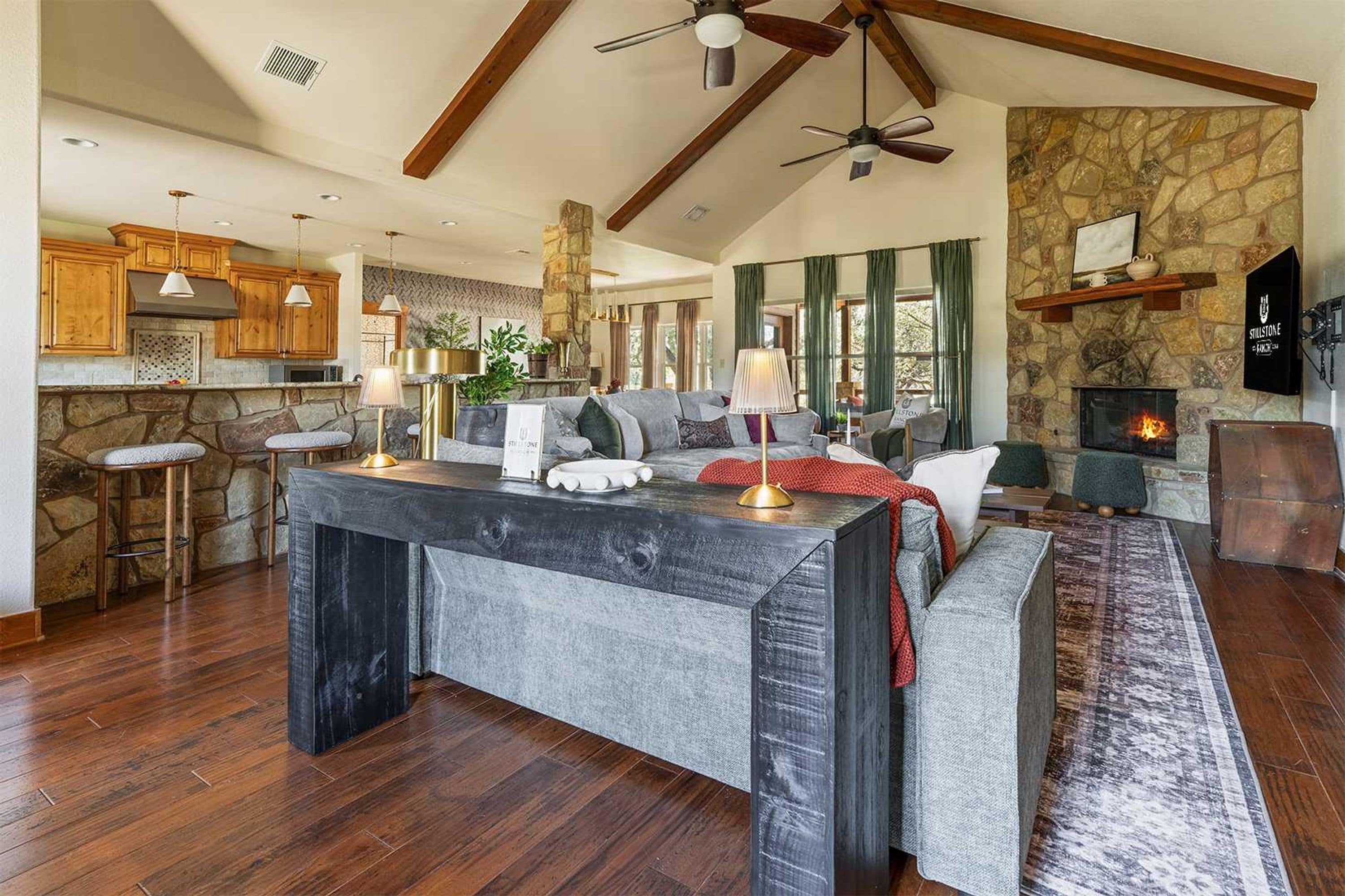 A spacious living area with a stone fireplace, a large island table, and a high ceiling with exposed beams.