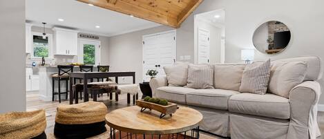 A modern living room with a wooden ceiling, a sofa set, a round coffee table, and a dining area with a table and chairs.