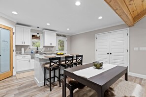 A modern kitchen with white cabinets, a central island, and a dining area with a bench and chairs. - MTN Views Hot Tub Games Dog Friendly (Ellijay)