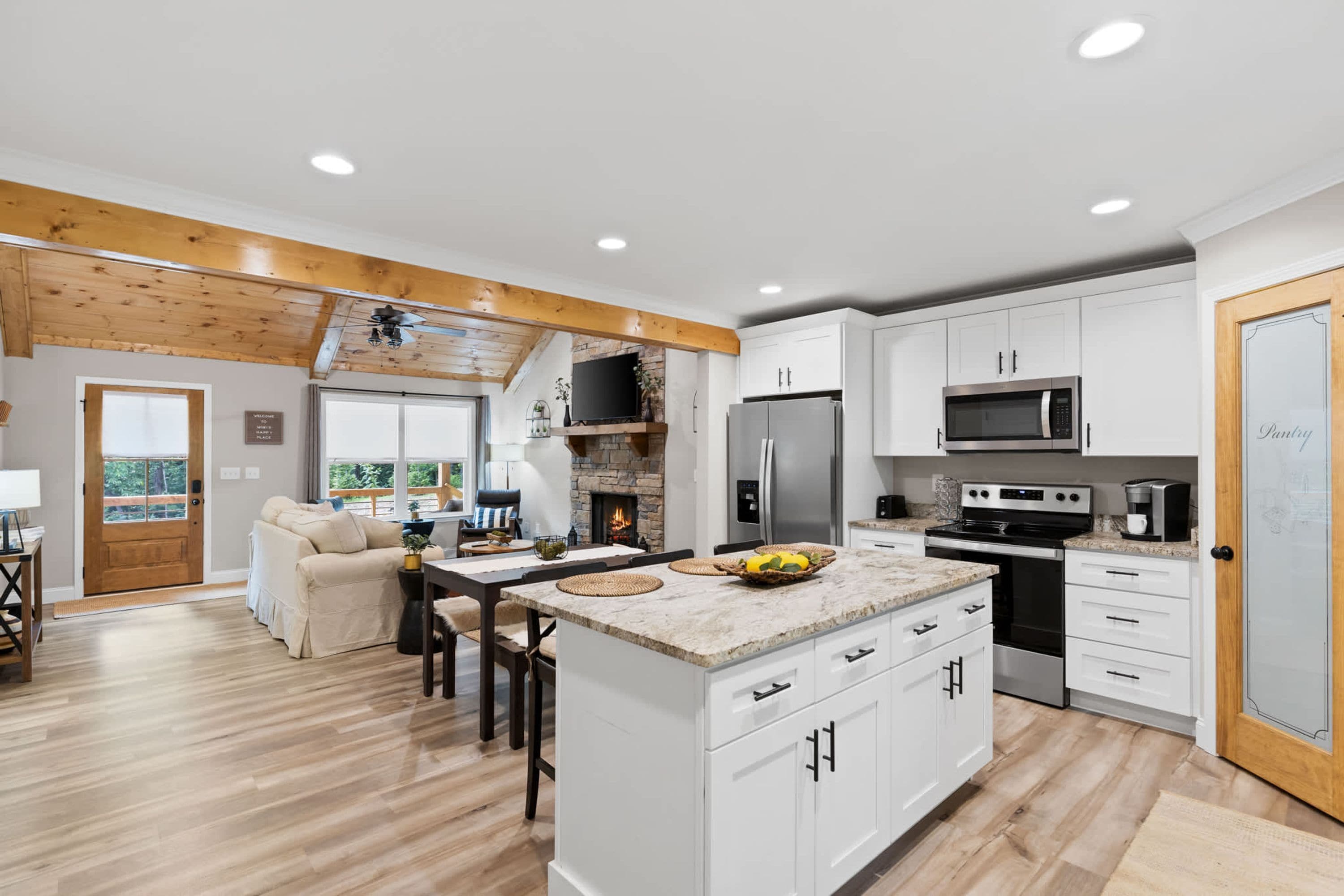 A modern kitchen with white cabinets, a central island, and a stone fireplace.