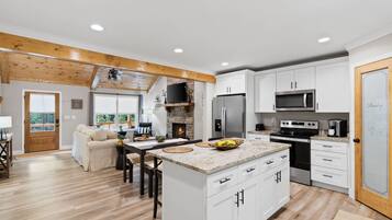 A modern kitchen with white cabinets, a central island, and a stone fireplace.