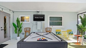 Una mesa de billar con bolas de billar, un televisor con la etiqueta 'Home Team' y asientos exteriores con sillas y mesas.