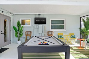 A pool table with billiard balls, a television labeled 'Home Team,' and outdoor seating with chairs and tables. - Epic Backyard - Pool - Hot Tub - Outdoor Theatre (Bradenton)
